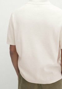 Korte mouw poloshirt in lichtcrème, gemaakt van textuurstof. Heeft een standaard kraag en een rechte zoom met een ontspannen pasvorm.