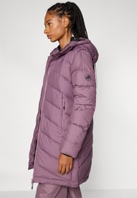 Puffjacka i ljuslila, med dragkedjestängning, huva, sidofickor och logotypdetalj på ärmen. Vadderad textur genomgående.