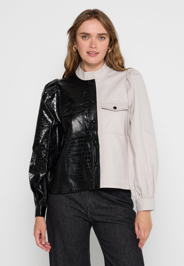 Asymetryczna kurtka z czarną stroną wykończoną kroko i jasnoszarym materiałem po drugiej stronie. Posiada bufiaste rękawy i zapięcie na zatrzask.