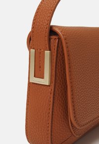 Braune Lederhandtasche mit strukturierter Oberfläche, ausgestattet mit einem goldfarbenen Metallakzent und einer klar definierten Form.