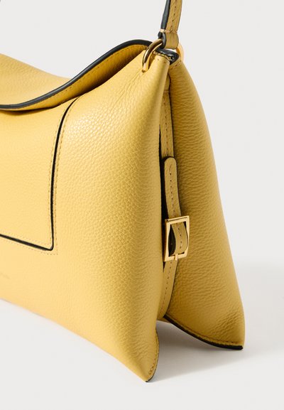 Dzeltens teksturēts ādas rokassomas ar melnām malām, zelta sprādzes detaļu un strukturētu trapecveida formu, attēlots sānos uz baltas fona.