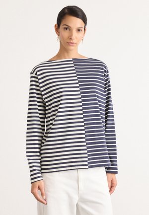 Stripet langermet skjorte med delt design: marineblå og hvite striper på den ene siden, i kontrast til ensfarget marineblå på den andre. Mykt stoff.