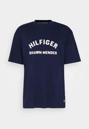 T-shirt bleu marine manches courtes avec texte blanc "HILFIGER" au-dessus de "SHAWN MENDES" sur le devant, col rond.
