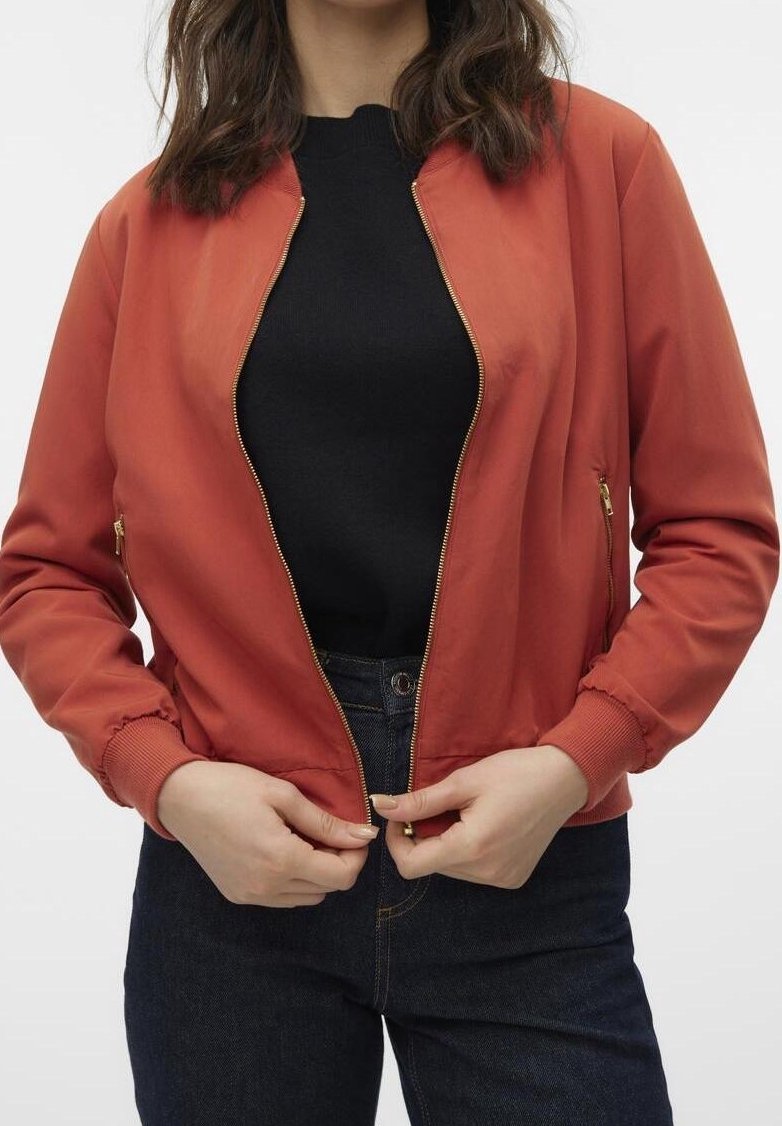 Veste bomber rouge avec fermeture éclair à l'avant, poignets côtelés et poches latérales. Portée sur un haut noir, assortie à un jean denim foncé. Texture lisse.