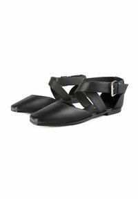 Pantofii plate din piele neagră au vârful ascuțit, un design cu curea încrucișată și o cataramă ajustabilă pentru o potrivire perfectă. Textura netedă și stilul minimalist.
