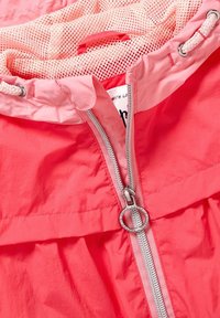 Giacca rosa brillante con zip argentata, caratterizzata da un tirante circolare, fodera in rete e cordino intrecciato vicino al colletto.