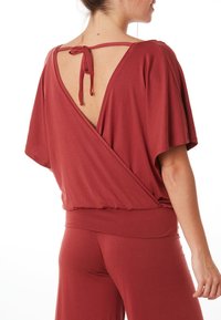 Lässiger, tiefroter Oberteil mit einer Rückenschleife, breiten Ärmeln und einer V-förmigen Rückenöffnung, aus einem weichen Stoff gefertigt.