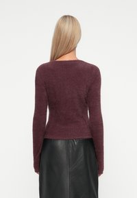 Bordeauxfarbener Strickpullover mit strukturiertem Finish, schmaler Passform und langen Ärmeln. Der Rücken hat einen Rundhalsausschnitt und einen leicht verkürzten Saum.