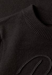 Gros plan d’un pull noir tricoté avec un col rond côtelé et un cordon tressé noir sur la surface du tissu.