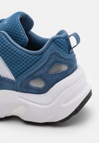 Modré sportovní tenisky vyrobené z nylonu a semiše, s tlustou bílou podrážkou, texturovanými akcenty a černou gumovou podrážkou.