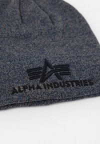 Navy knit beanie made from textured fabric, featuring a black embossed logo and brand name stitched along the hem.