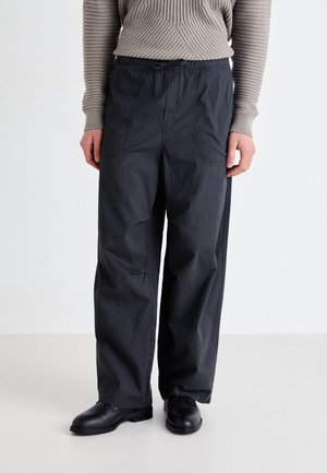 Zwarte, loszittende broek met een elastische tailleband en trekkoord. Gemaakt van lichtgewicht stof, voorzien van zijzakken en subtiele stiksels.