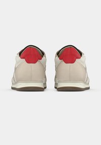 Μπεζ αθλητικά παπούτσια με κόκκινες λεπτομέρειες στη φτέρνα και μαύρη επένδυση. Κατασκευασμένα από δέρμα και ύφασμα, με υφή στην επιφάνεια και ελαφριά σόλα.