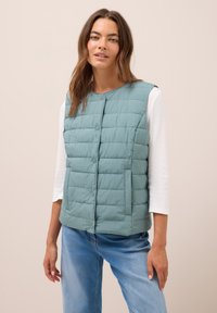 Ljus teal-färgad puffer-vest med rund halsringning, knappstängning och två sidofickor. Quilltad textur och lättviktsdesign, bärs över en vit topp.