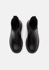 Bottes noires à la cheville avec une texture crocodile, des panneaux latéraux élastiques et un intérieur rembourré. Semelle en caoutchouc robuste avec des bords crantés.