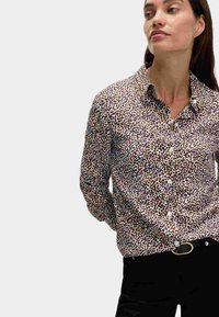 Camisa de botones con un estampado abstracto de animales en tonos marrón y crema, de mangas largas y con cuello, hecha de tela ligera.