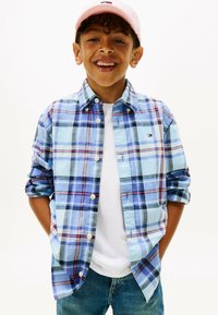 Knoop-up geruite shirt in lichtblauw, met donkerblauwe en roze patronen. Gecombineerd met een wit T-shirt en denim jeans.