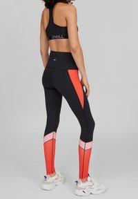 Czarne legginsy sportowe z pomarańczowymi i różowymi akcentami, wysoka talia i dopasowany krój; w połączeniu z czarnym biustonoszem sportowym i białymi sneakersami.
