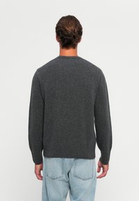 Mörkgrå stickad tröja med rund halsringning, långa ärmar och ribbad nederkant. Bärs tillsammans med ljusblå jeans som har en avslappnad passform.