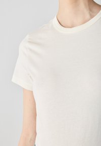 Cotton t-shirt in off-white with short sleeves, a crew neckline, and contrasting light trim at the collar and sleeve edges. Smooth texture.