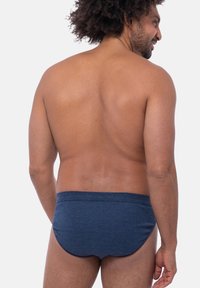 Slip da bagno blu a righe con una texture liscia, cintura elastica e una forma aderente, mostrato da un angolo posteriore su un modello.