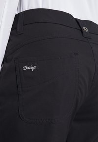 Svarta byxor med en bakficka som har broderad text "Daily", tillverkade av ett mjukt tyg som framhäver rena linjer och subtila sömmar.