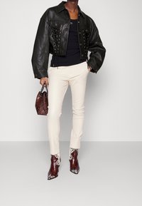 Svart croppad skinnjacka med snörningsdetalj, kombinerad med krämfärgade slim-fit byxor och bruna ankelboots med ormskinnsmönster. Brun väska med handtag.