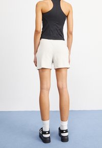 Svart åtsittande linne i kombination med ljusbeige ribbade shorts. Bärs med svarta träningsskor och vita ankelsockar. Enkelt, minimalistiskt design.