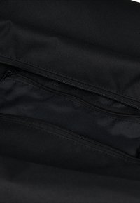 Interno di una borsa nera in tessuto caratterizzato da una superficie liscia, molteplici scomparti con cerniera e un design minimalista privo di abbellimenti.