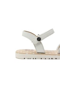 Sandal in pelle bianca con suola piatta. Presenta cinturini incrociati e una soletta beige decorata con stelle. Include un accento hardware decorativo.