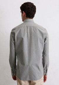 Chemise boutonnée grise avec de fines rayures blanches, à manches longues, coupe ajustée et poignets boutonnés. Tissu lisse avec un design de col classique.