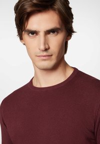 Bordowy sweter z dzianiny z okrągłym dekoltem, dopasowanym krojem i ściągaczami na rękawach. Tekstura wydaje się gładka i jednolita przez cały czas.