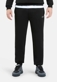 Zwarte katoenen sweatpants met elastische tailleband en boorden. Kenmerkt zich door een klein gekleurd logo op de linkerdij. Draagt met zwarte sportschoenen.