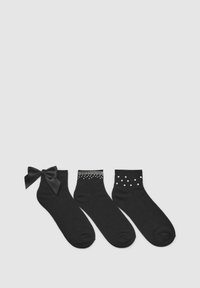 Trzy pary czarnych skarpetek: jedna z satynową kokardą, jedna z srebrnymi wkrętami i jedna w białe kropki, wszystkie z miękkiego materiału.