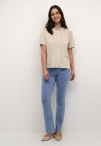 Beige linned skjorte med korte ærmer og flæsekrave, knaplukning foran; parret med lyseblå smalle jeans og nude hæle. Glat stofstruktur.