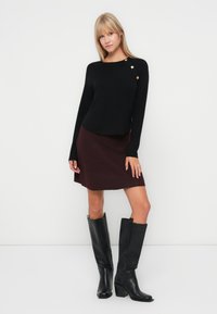 Pull noir à col rond avec des détails de boutons dorés, associé à une jupe bordeaux et des bottes en cuir noir jusqu'au genou. Texture lisse dans l'ensemble.