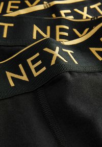 Crne bokserice s širokim crnim pojasom na kojem je u sjajnom zlatnom slovu napisano "NEXT". Glatka tekstura, elastičan materijal.