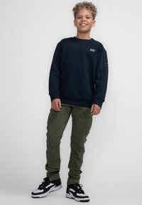 Marineblauwe sweatshirt met lange mouwen, geribbelde manchetten en zoom; olijfgroene cargo broek met meerdere zakken; zwart-witte sneakers.