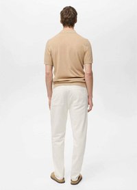 Beige polo tričko s krátkym rukávom a ribbed štruktúrou, spárované s bielymi nohavicami s dvoma zadnými vreckami. Jednoduchý, neformálny dizajn.