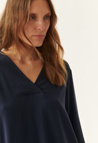 Top azul marino con escote en v de corte relajado, hecho de una tela suave, con mangas largas y un ligero detalle de textura en el escote.
