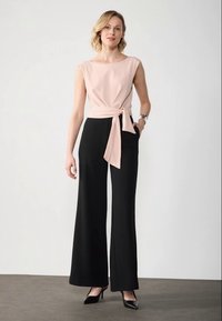 To-delt antrekk som har en lysrosa tettsittende topp med midjebånd og vide svarte bukser. Stoffet er glatt med en matt overflate.