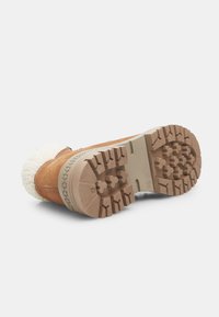 Bottes en cuir marron avec une semelle texturée couleur sable, dotées d'un accent en fourrure blanche en haut et d'un motif de semelle robuste pour une meilleure adhérence.