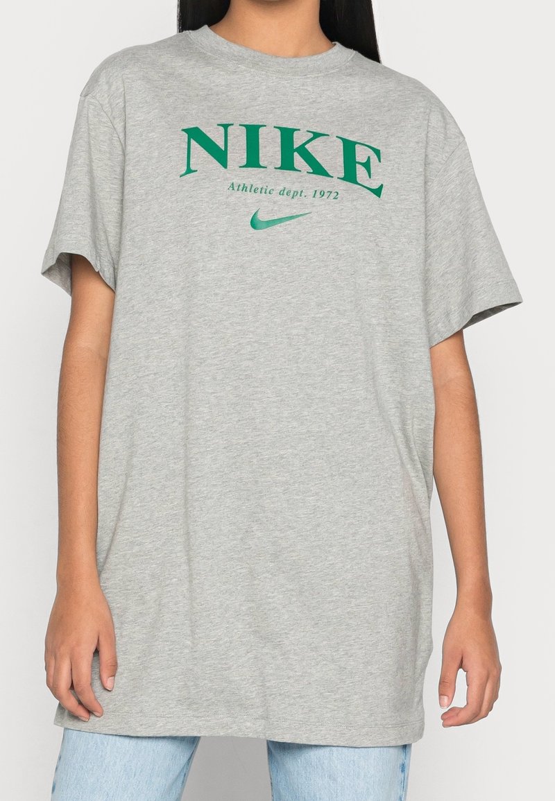 Camiseta gris de gran tamaño hecha de algodón, con un logo verde de Nike y texto. Manga corta y un corte relajado con un cuello redondo.