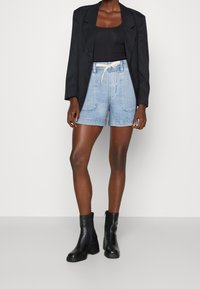 Ljusblå denimshorts med elastisk midja och dragsko, kombinerat med en svart tajt topp och svarta ankelskor.