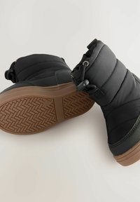 Schwarze isolierte Knöchelstiefel mit gepolstertem Schaft, Gummisohle und strukturiertem Grip-Muster. Verfügt über eine verstellbare Schnürung und Schlaufe für ein einfaches Anziehen.