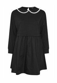 Musta mekko pitkillä hihoilla, kerroksella varustettu hame ja pyöreä valkoinen kaulus. Takana avaus avaimenreiällä. Pehmeä, teksturoitu kangas.