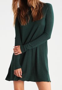 Grön långärmad klänning med en avslappnad passform, mjuk textur och en nederkant som svagt flädrar. Har figursydda ärmar och rund halsringning.