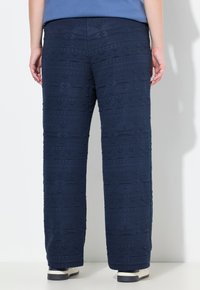 Pantaloni larghi a righe navy con motivi geometrici, realizzati in morbido tessuto. Presentano una vita liscia e si fermano alla caviglia. Abbinati a sneakers.