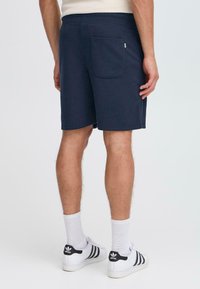 Shorts en coton navy avec taille élastique et une poche arrière, présentant un design simple et une texture douce. Portés avec des chaussettes blanches et des baskets.