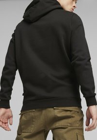 Sudadera negra con puños acanalados, capucha y un corte relajado, combinada con pantalones cargo verde oliva que cuentan con bolsillos laterales y una textura suave.